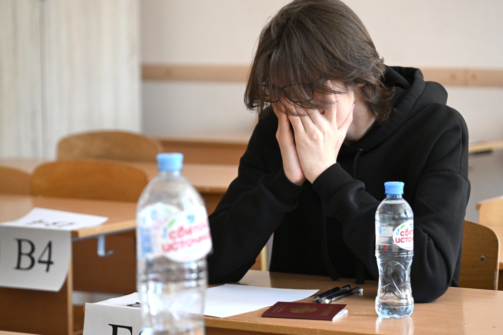 Парень в черной толстовке за партой с бутылкой воды.