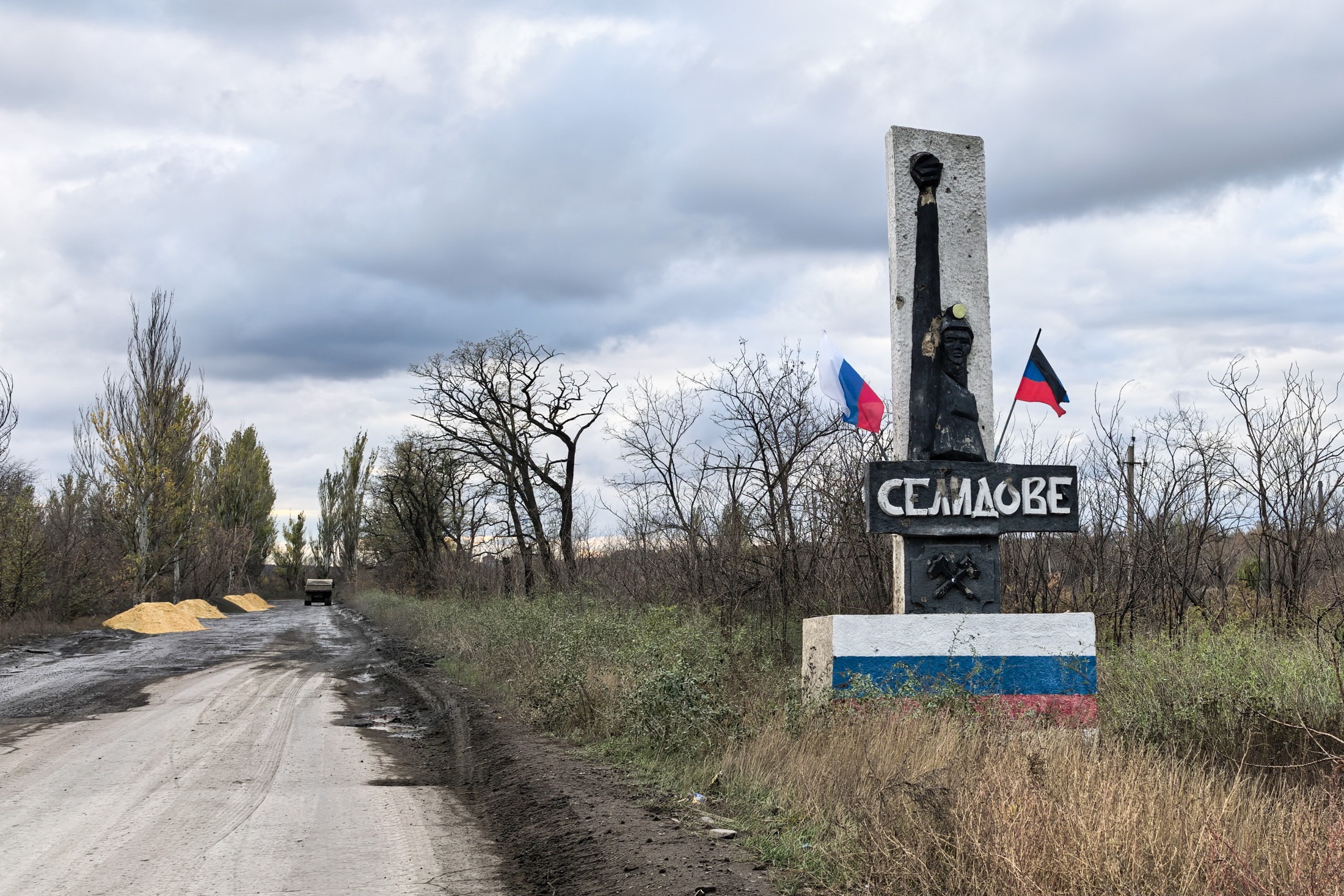 Надпись при въезде пока оставили на украинском языке. А вот флаги украшают стелу российские.