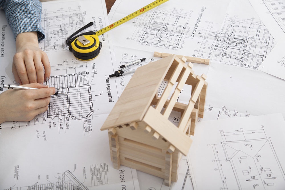 Многие задаются вопросами: "как спроектировать дом, который "растет" вместе с семьей" и "как построить частный дом по этапам, чтобы въехать быстрее? Человек чертит чертеж, план cстроительства будущего дома