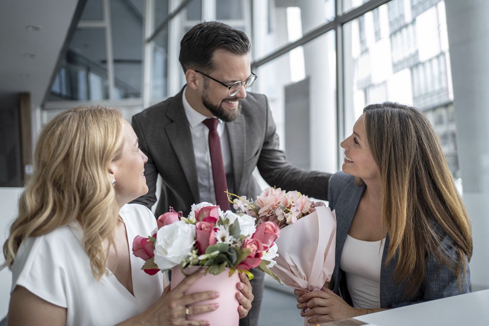 Мужчина дарит коллегам женщинам букеты цветов на 8 Марта. 