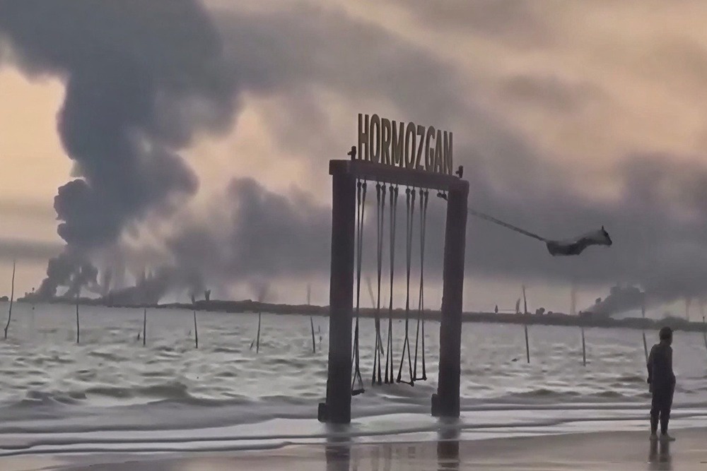 Неизвестная иранская девочка на качелях. За ее спиной охваченная огнем военно-морская база.