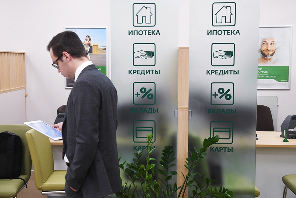 Страхование вкладов защищает деньги клиентов банка, если у последнего отозвали лицензию. Мужчина проходит мимо стеклянной стены с вывесками про ипотеку, вклады и кредиты в банке